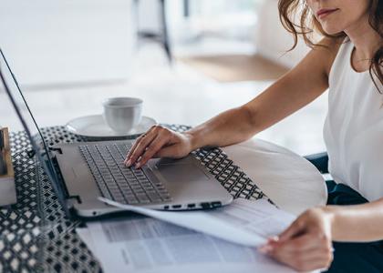 Image of a woman reading paperwork with a laptop