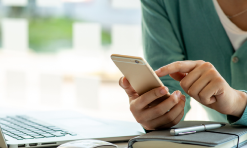 A close up of a person using a phone next to a laptop.